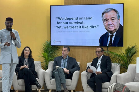 A presenter standing in front of an audience, with other panel members at the background, during an event at the Restoration Pavilion, on 4 December 2024, in Riyadh, Saudi Arabia