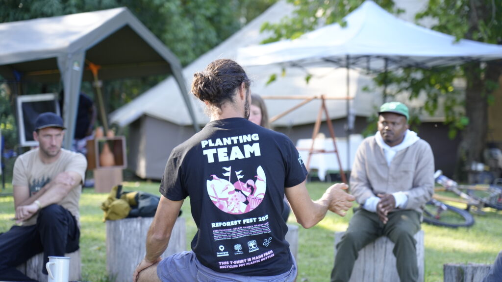 A man with Planting Team text on the back of his t-shirt in a discussion group at Reforest Fest 2025