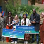 A group of winners and hosts together, holding prizes of large cards for 10,000 USD