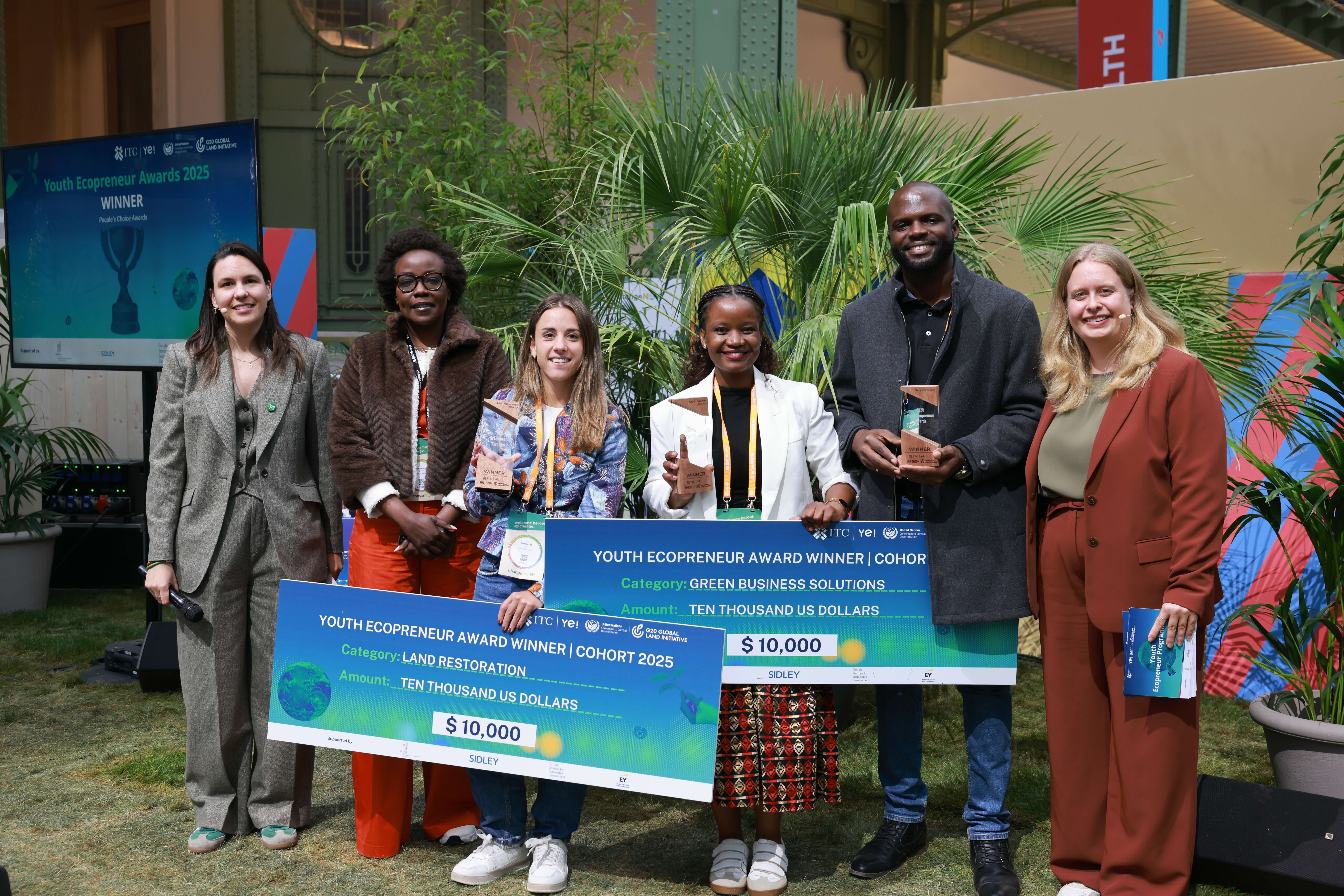A group of winners and hosts together, holding prizes of large cards for 10,000 USD