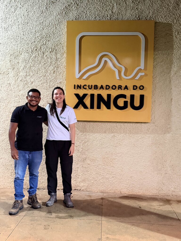 Two people standing in front of the Incubadora do Xingu sign